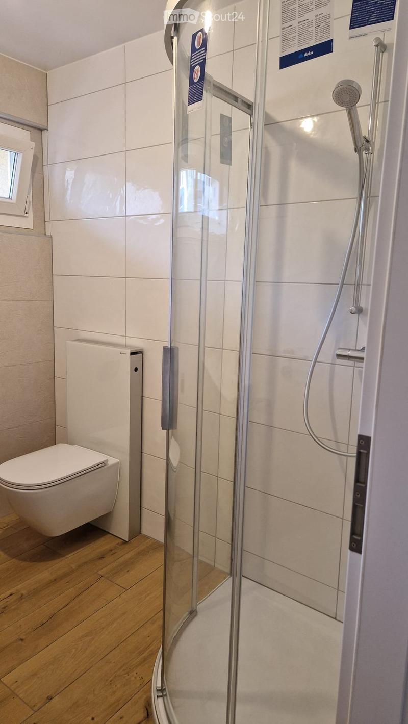 Modern bathroom with white tiled walls, a glass-enclosed shower, a toilet, and a handheld showerhead.