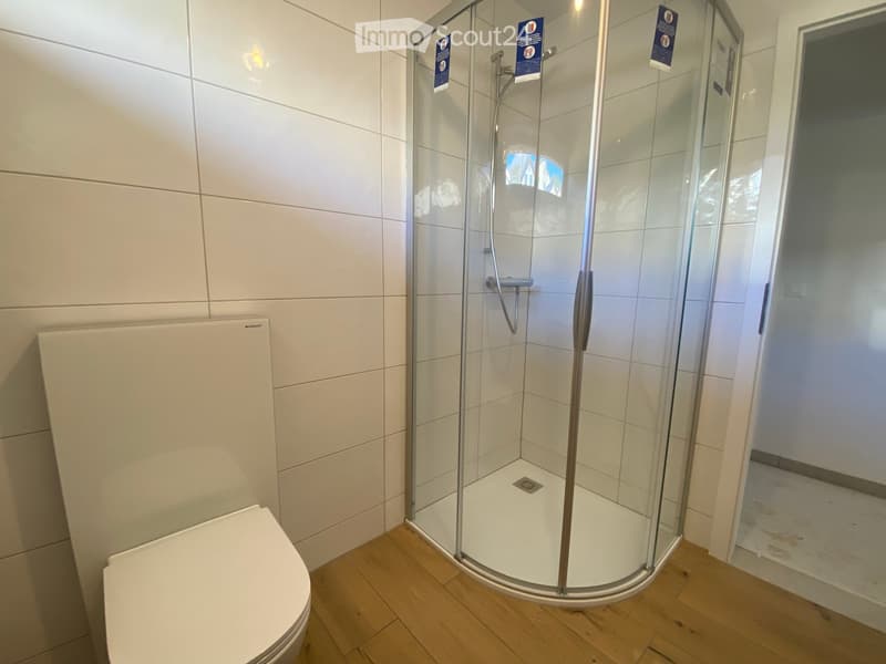 Modern bathroom with a white toilet, a glass-enclosed shower stall, and tiled walls.