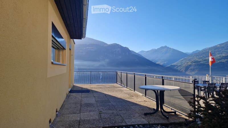 Balcony with a table and chairs, overlooking a scenic mountain and lake view.