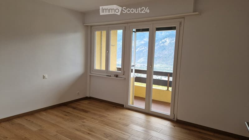 Empty room with wooden flooring, large sliding glass doors leading to a balcony with a scenic mountain view.