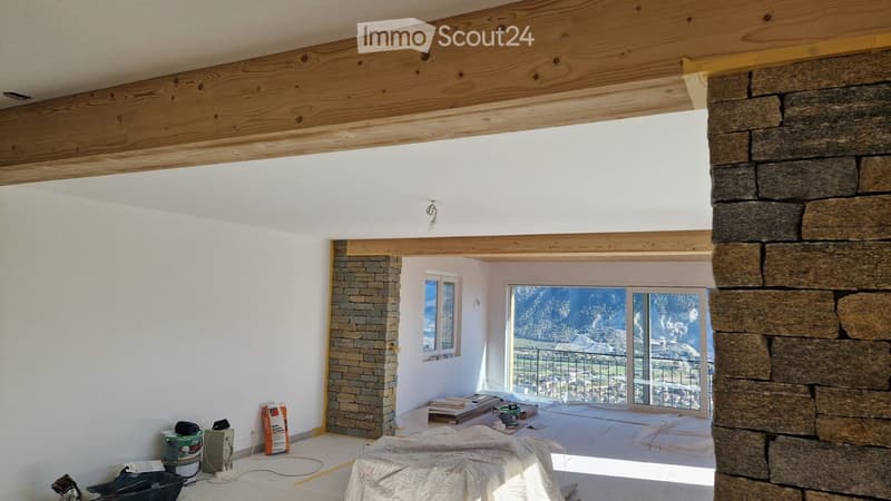 Empty room with exposed wooden beams, white walls, and a large window offering a scenic view. The floor is covered with protective sheets, and construction materials are visible near the window.