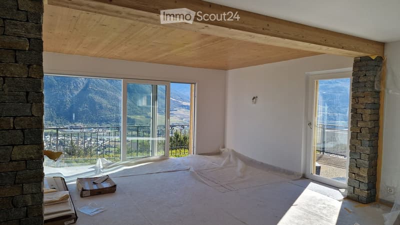 Empty room with large windows offering a scenic mountain view, wooden ceiling, and stone pillars.