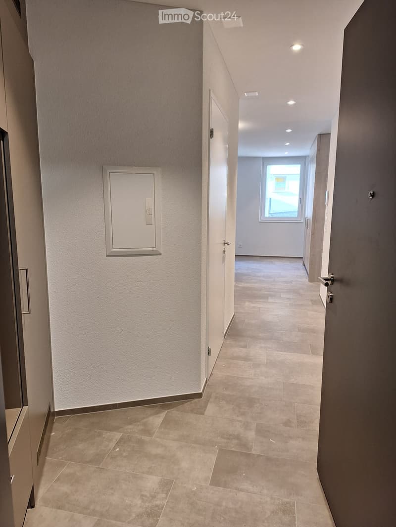 {"visible_features": [], "type": "Hallway", "description": "Empty hallway with white walls, beige tiles, an outlet frame, and an open door at the end. Two closed doors with knobs on the left and right side."}