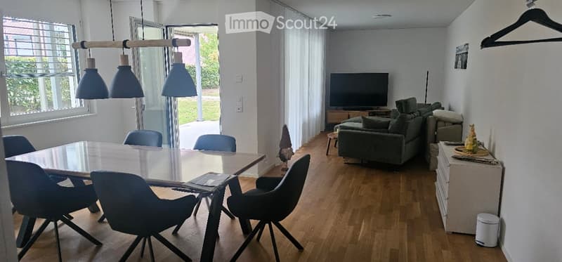 Open-plan living and dining area with modern furniture, large windows, and a view of the garden.