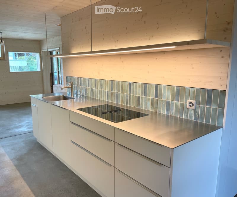 Modern kitchen with stainless steel sink, white cabinets, and a sleek countertop, featuring a large window and minimalist design.