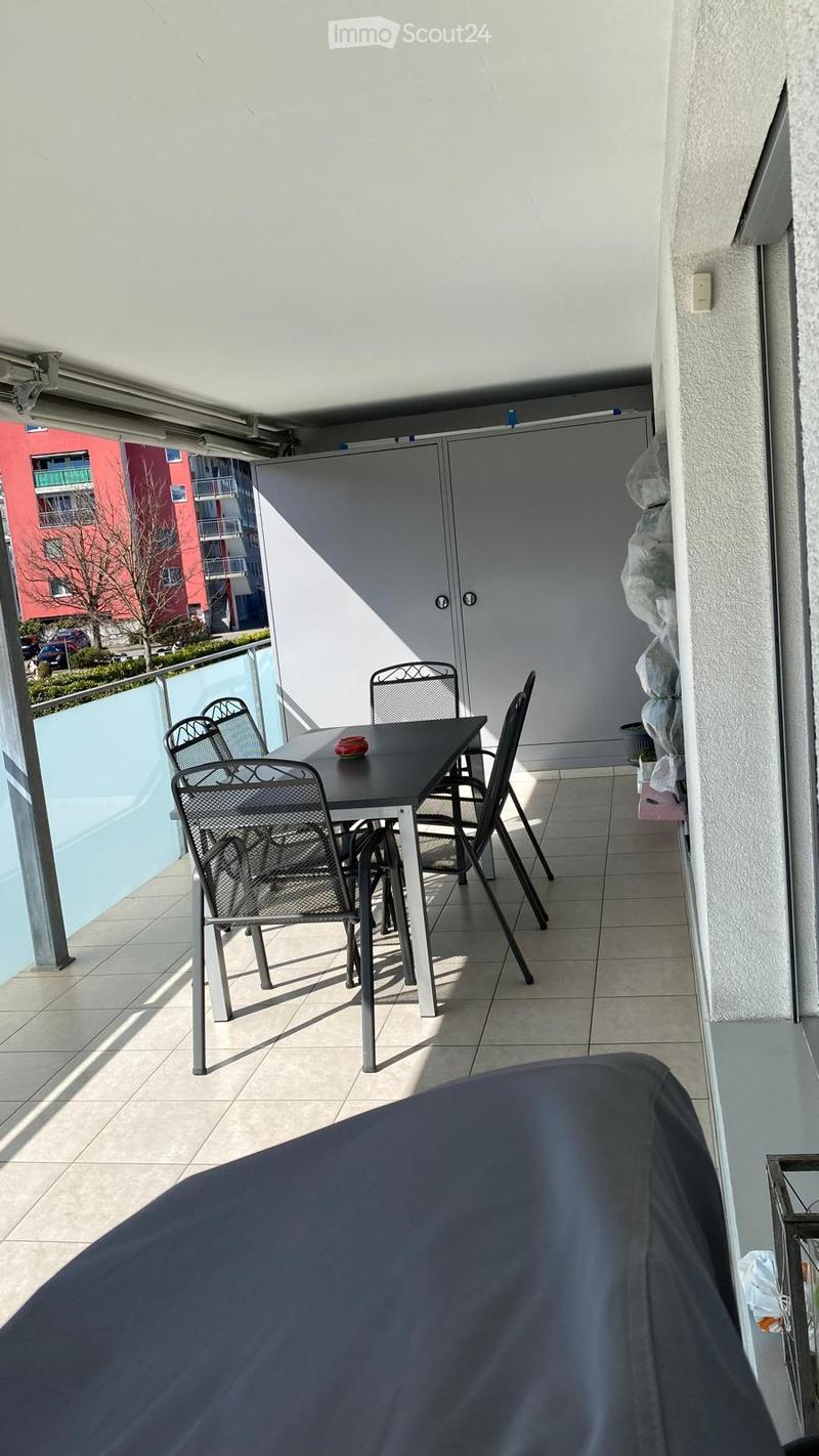 Balcony with tiled floor, table, and chairs, featuring a covered area and a view of the building.