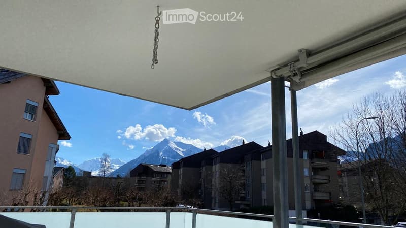 Balcony with a retractable roof, overlooking a cityscape with mountains in the background.