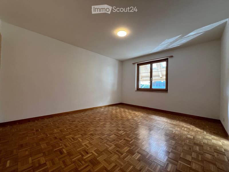 Empty room with wooden parquet flooring, white walls, and a single window with a brown frame. The ceiling has a recessed light fixture.
