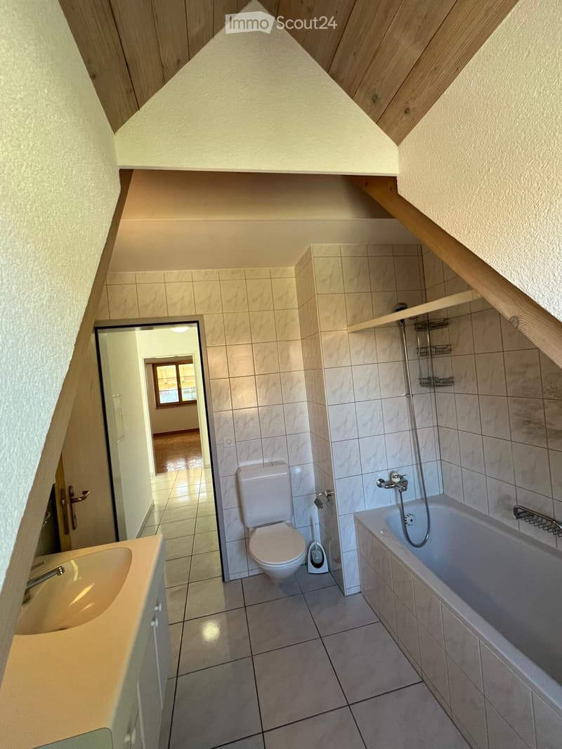 Bathroom with a toilet, bathtub, and sink, featuring tiled walls and a wooden ceiling with slanted beams.