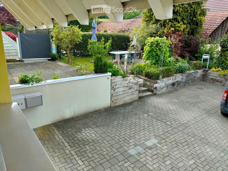 Garden area with a paved patio, raised garden beds, various plants, and a small seating area with a table and chairs.