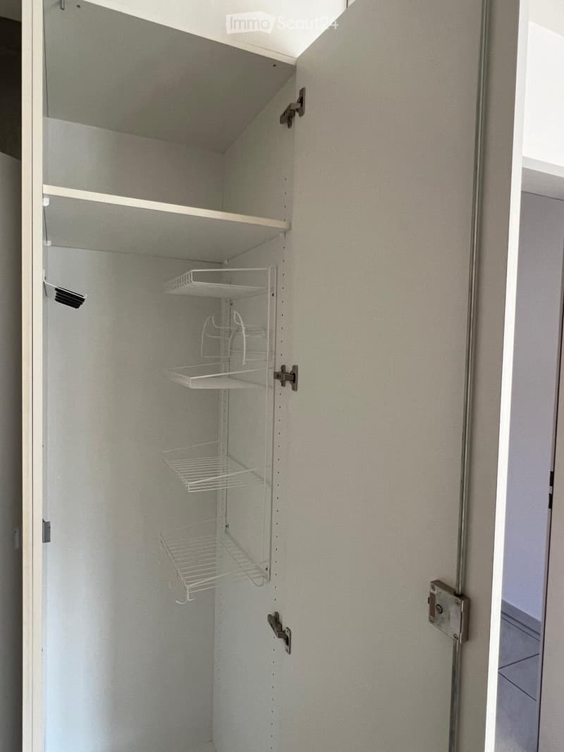 Empty closet with white shelves and a wire basket, grey walls, and a partially visible door frame.