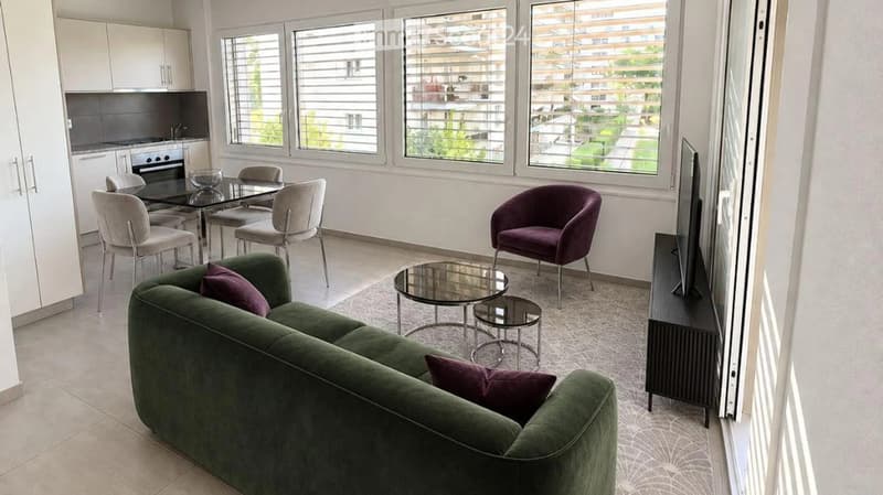 Modern living and dining area with a green sofa, coffee table, dining table, chairs, TV stand, and kitchen area with an oven and cabinets.