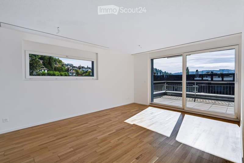 Empty room with wooden flooring, white walls, large window, and sliding glass doors leading to a balcony with a scenic view.