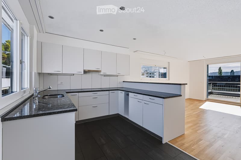 Modern kitchen with white cabinets, granite countertops, and a sink. Large windows offer a scenic view.