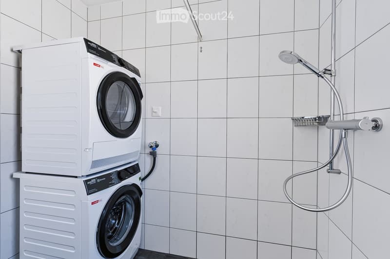 Modern bathroom with white tiled walls, a stacked washer and dryer unit, and a handheld shower head with a hose.