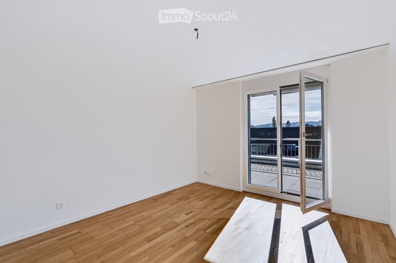 Empty room with wooden flooring, white walls, and a large sliding glass door leading to a balcony. A single bench is placed near the door.