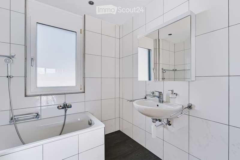 Modern bathroom with white tiles, a bathtub, a sink with a mirror, and a shower head.