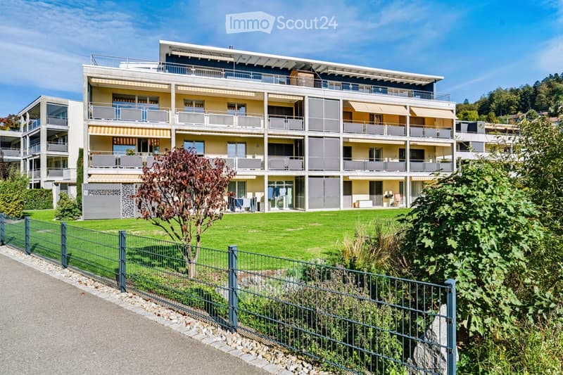 Modern multi-story residential building with balconies, large windows, and a well-maintained lawn in front.
