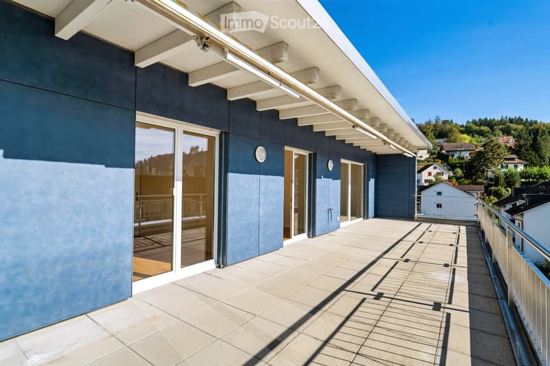 Modern balcony with tiled flooring, glass sliding doors leading to a room, white metal railing, and a view of a residential area with trees and houses.