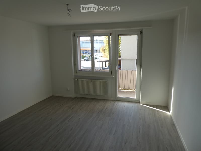 Empty room with wooden flooring, white walls, large windows, and a radiator. No furniture or equipment present.