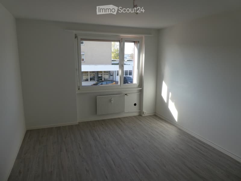 Empty room with wooden flooring, white walls, and a large window with a radiator below it.