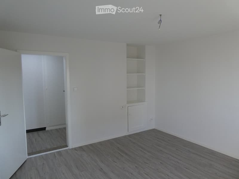 Empty room with light-colored walls, wooden flooring, and a built-in shelving unit with empty shelves.