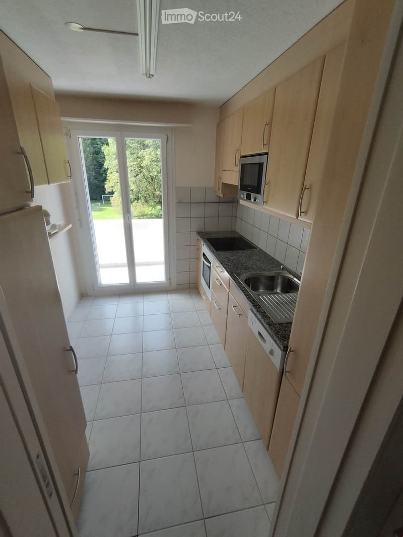Modern kitchen with light wooden cabinets, granite countertop, stainless steel sink, microwave, and oven. Large sliding glass door leads to outdoor area.