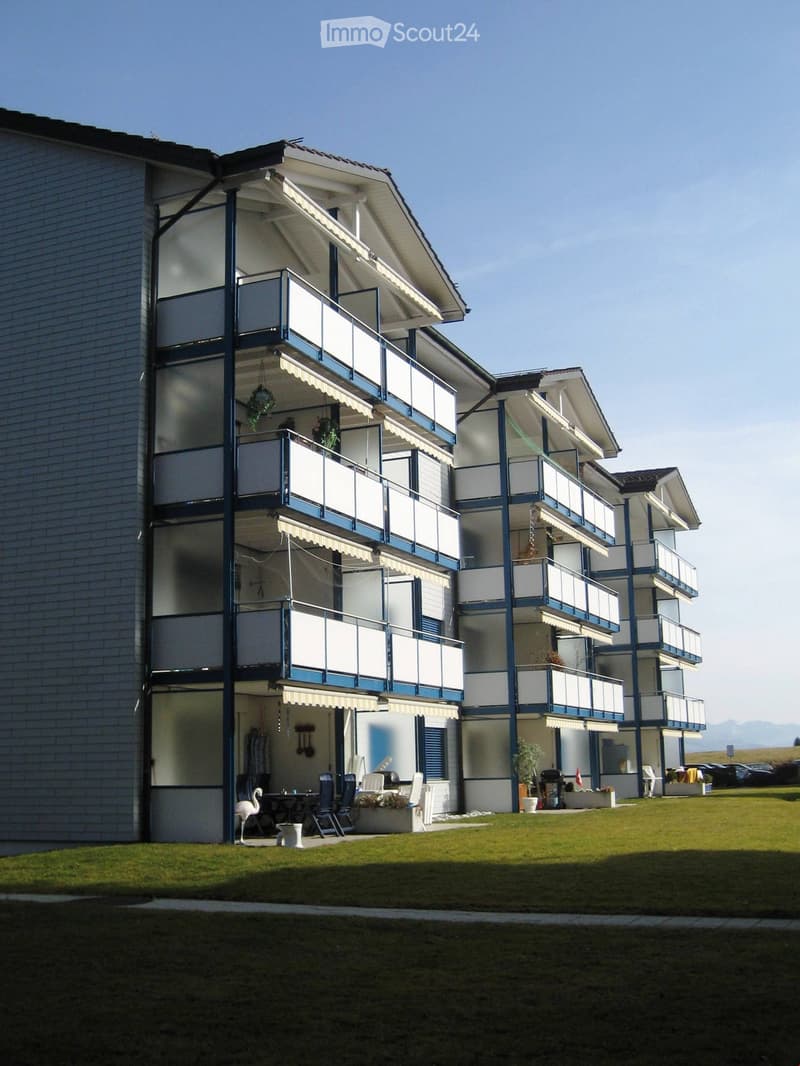 Multi-story residential building with balconies, awnings, and outdoor seating area.
