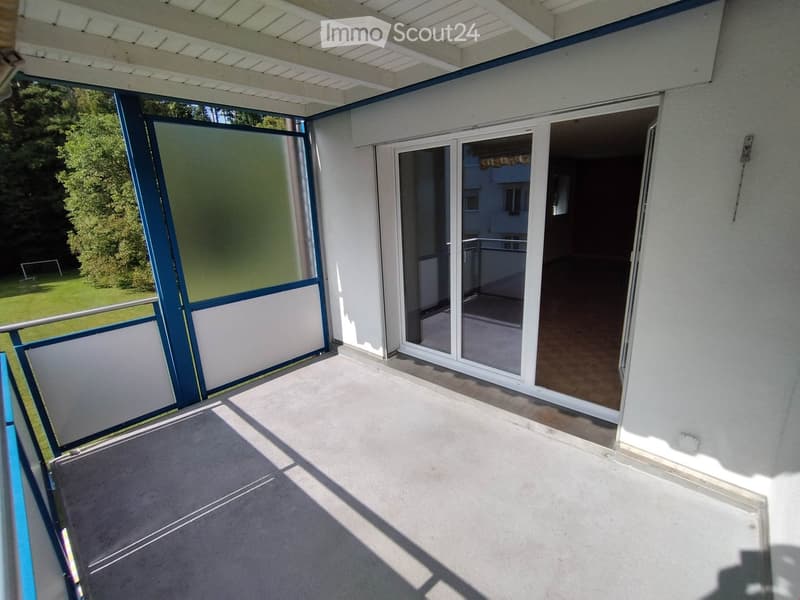 Balcony with sliding glass doors, white walls, and a view of a green lawn and trees.