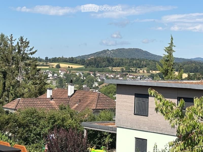 View of a residential area with houses, trees, and a distant mountain range under a clear blue sky.