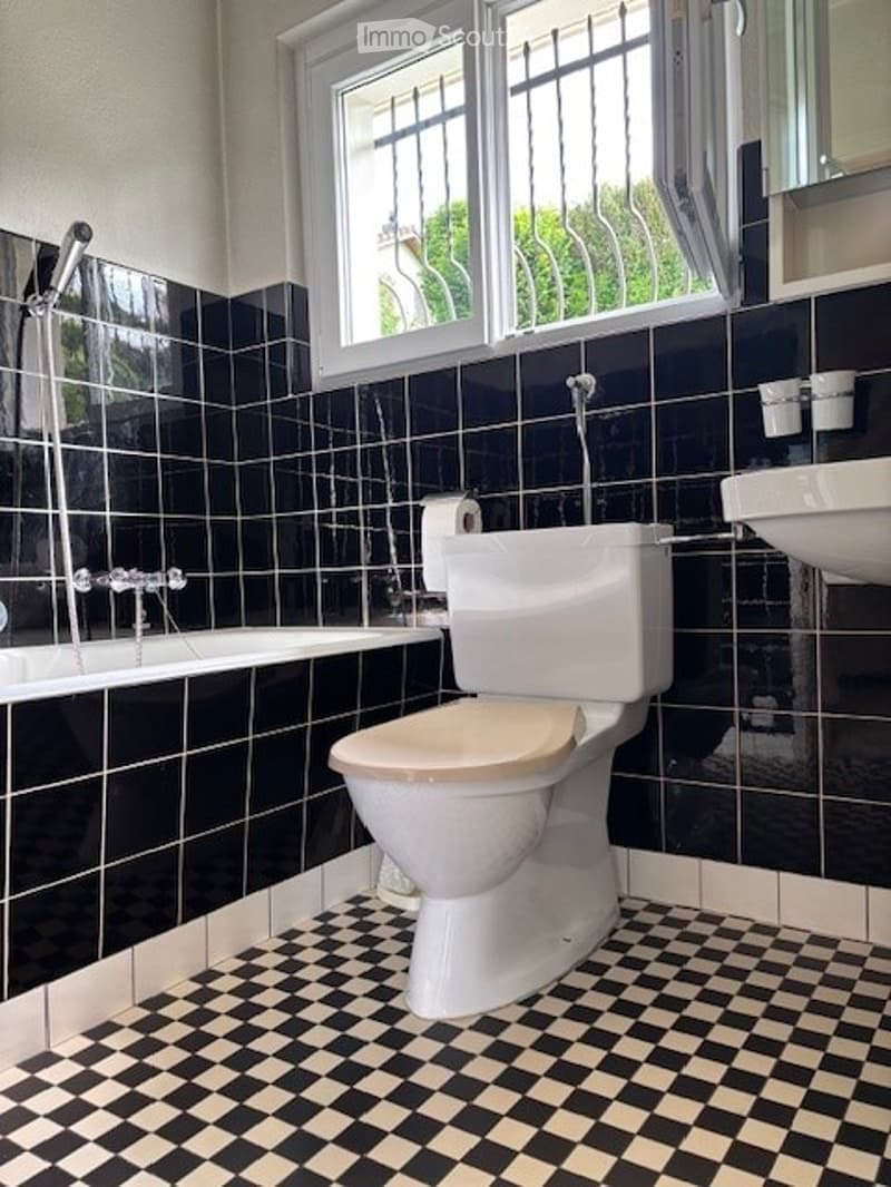 Bathroom with black tiled walls, checkered floor, toilet, bathtub, sink, and mirror.