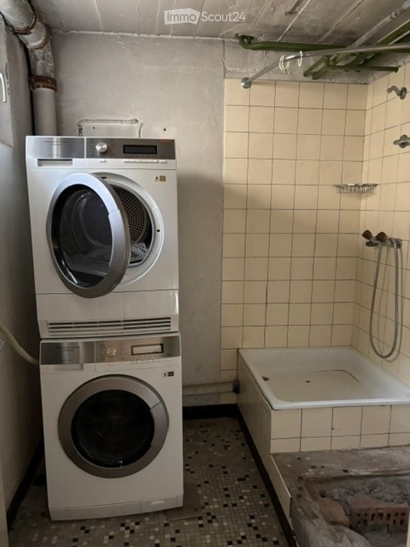 Bathroom with a bathtub, washing machine, and dryer. The walls are tiled, and the floor has a mosaic tile pattern.