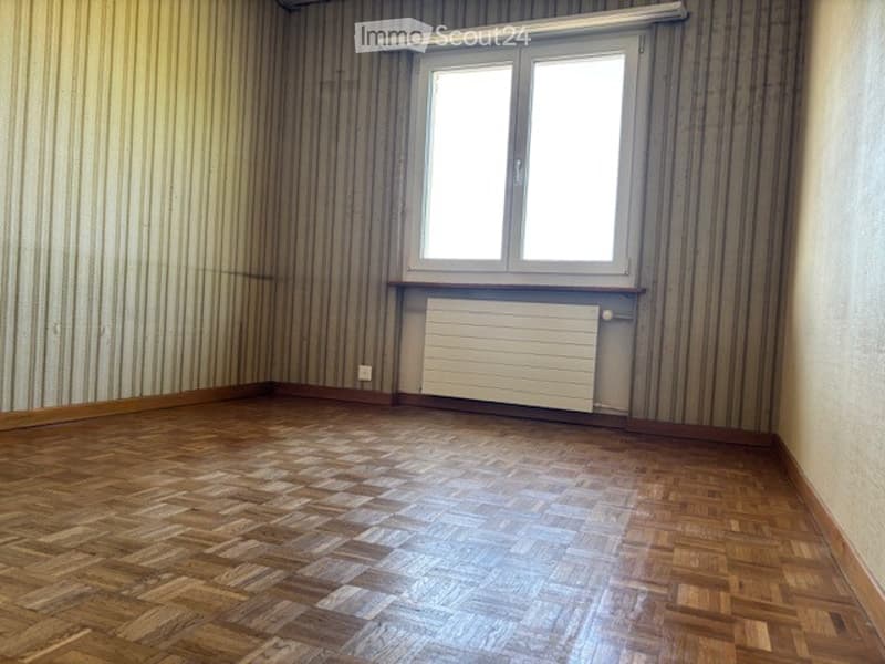Empty room with wooden flooring, striped wallpaper, a window with white frame, and a radiator below it.