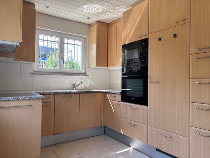 Modern kitchen with light wooden cabinets, granite countertops, and built-in microwave and oven. Features a window above the sink and a tiled backsplash.