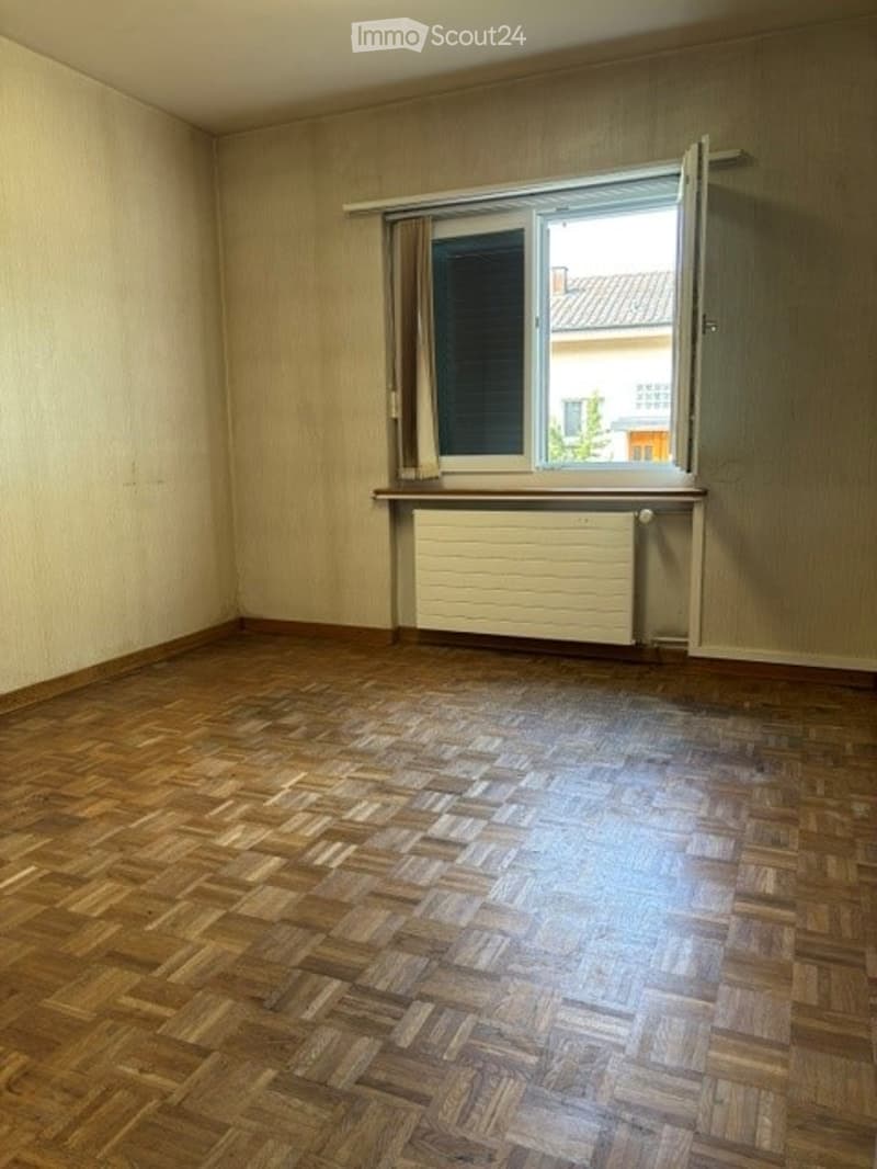 Empty room with wooden parquet flooring, light-colored walls, and a window with white radiator below. No furniture or equipment present.