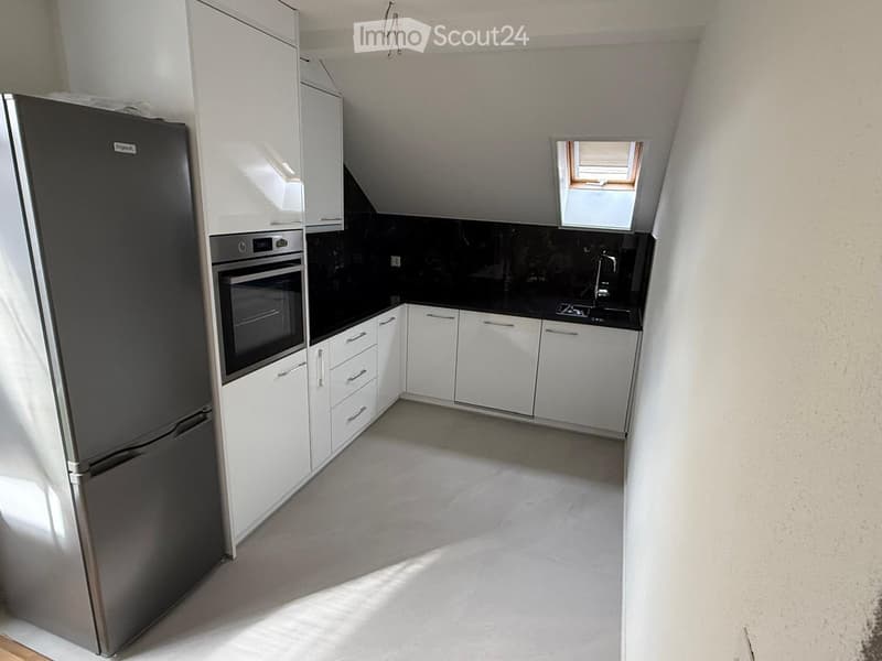 Modern kitchen with white cabinets, stainless steel refrigerator, oven, and sink, featuring a black countertop and a small window above the sink.