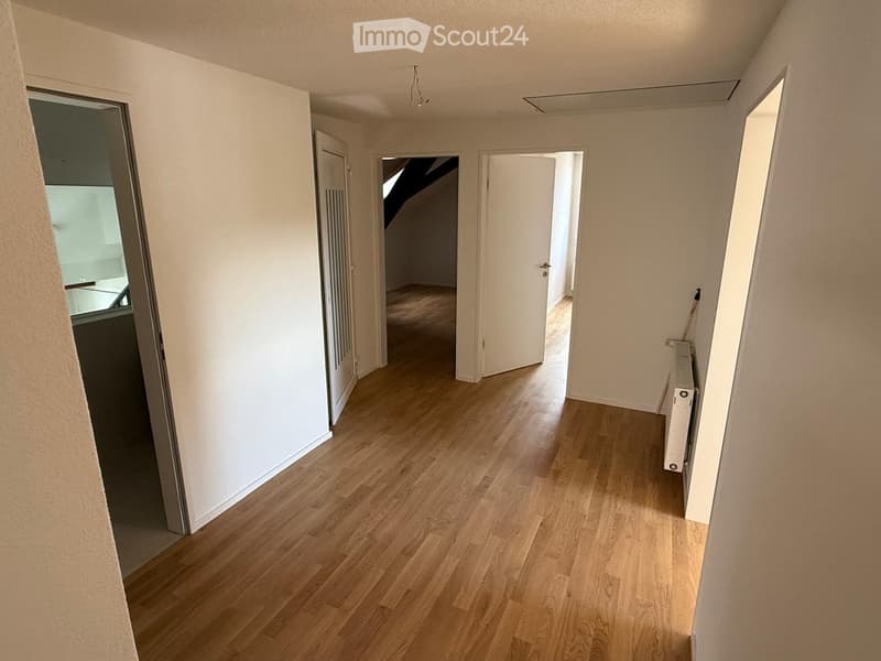 Empty hallway with wooden flooring, white walls, and several open doors leading to other rooms.