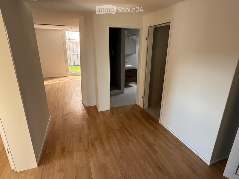Empty hallway with light wooden flooring and white walls, featuring open doors leading to other rooms.