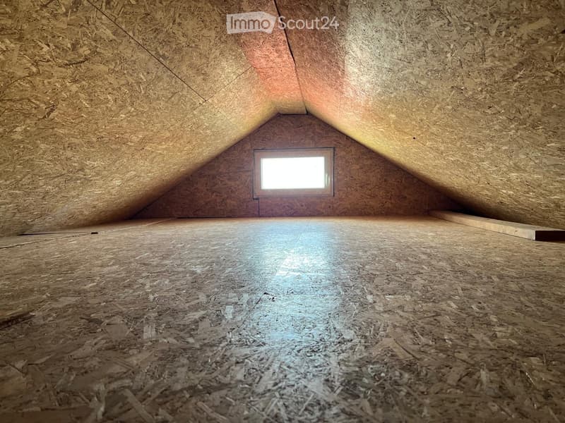 Empty attic space with wooden walls, floor, and a single window letting in natural light.