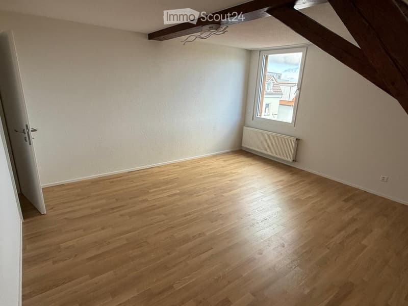 Empty room with wooden flooring, white walls, a window with a view, and a radiator. No furniture or equipment present.