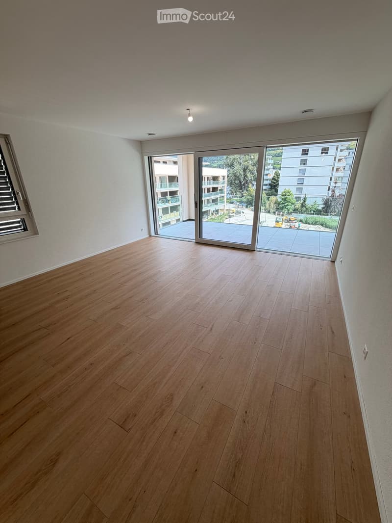 Empty room with wooden flooring, large sliding glass doors leading to a balcony, and white walls.