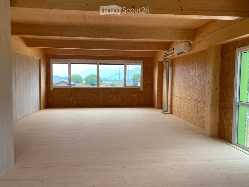 Empty room with wooden walls, ceiling, and floor, large windows with scenic view, exposed wooden beams, and visible ventilation ducting.