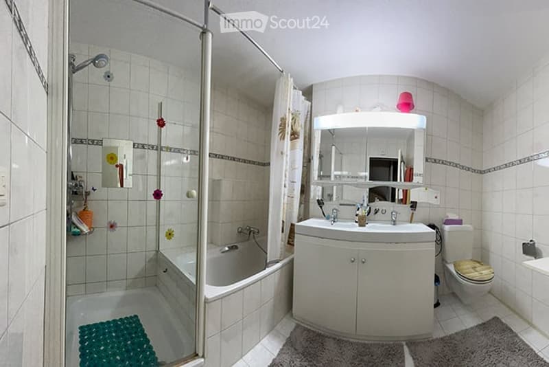Bathroom with a bathtub, sink, toilet, mirror, and cabinet. Shower area with a curtain and shower head. Tiles on walls and floor, with decorative elements like a bath mat and small flowers.