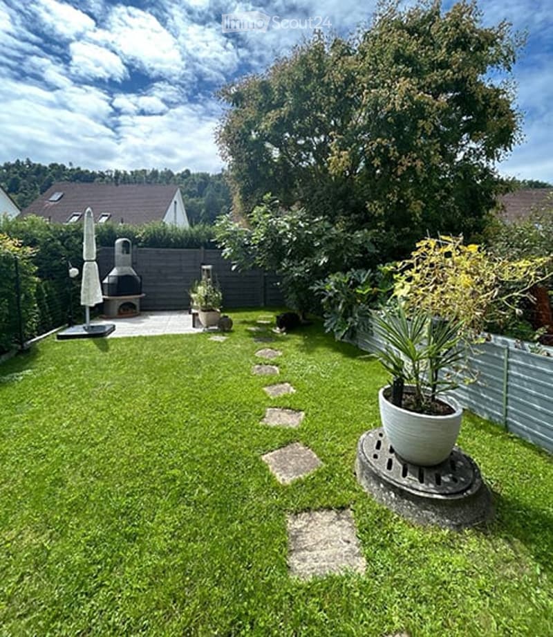 Well-maintained garden with a lawn, stepping stones, potted plants, and a barbecue area with an umbrella.