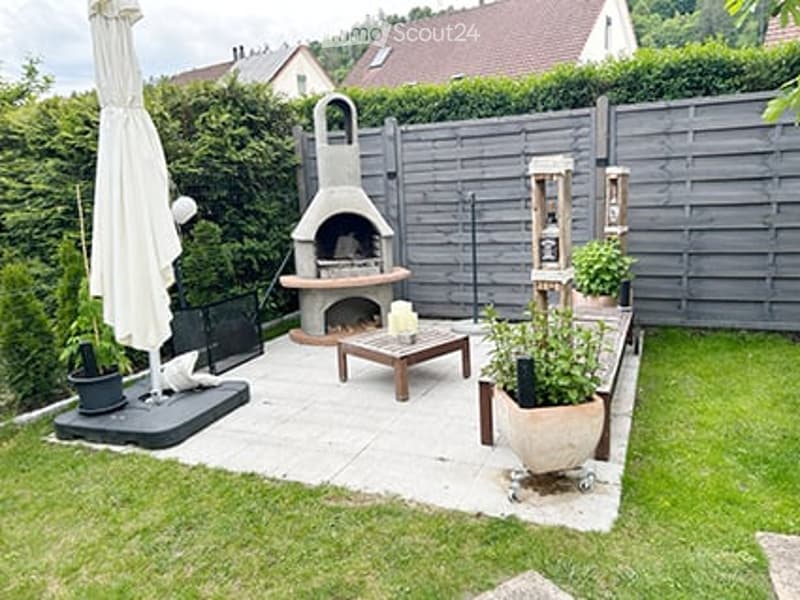 Well-maintained garden with a patio area, outdoor furniture, a barbecue, and potted plants.
