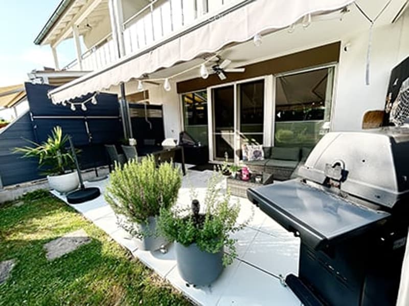 Outdoor patio with a covered awning, potted plants, a grill, and seating area.