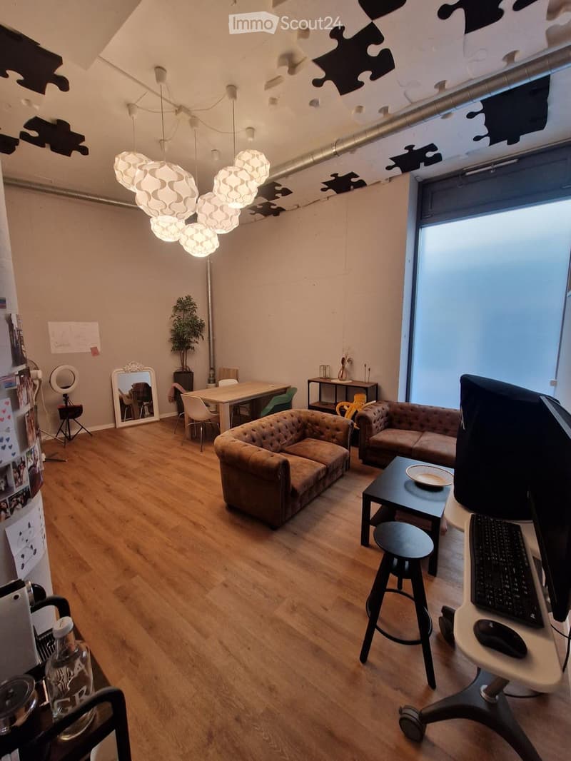 A modern living room with wooden flooring, two sofas, a coffee table, a dining table with chairs, a mirror, a plant, and a desk with a laptop and screen.