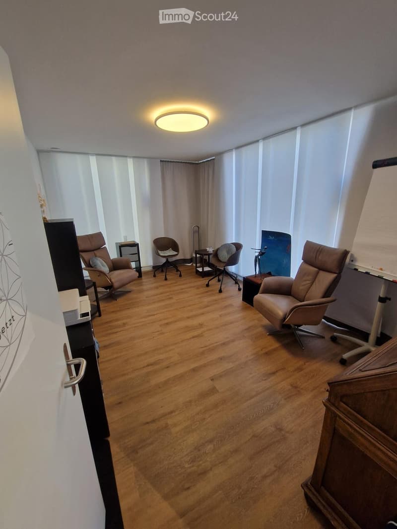 A well-lit room with wooden flooring, featuring several chairs, a small table, and a cabinet.