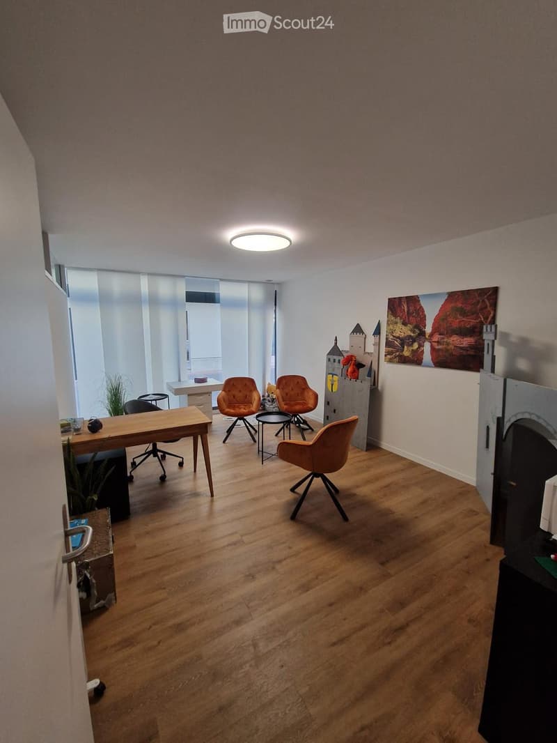 Modern office space with wooden flooring, large window, round desk, chairs, small table, and decorative castle structure.
