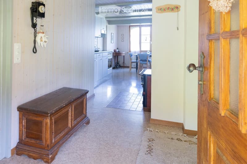Hallway with wooden walls, a wooden bench, and a view into a kitchen area with cabinets, a table, and chairs.